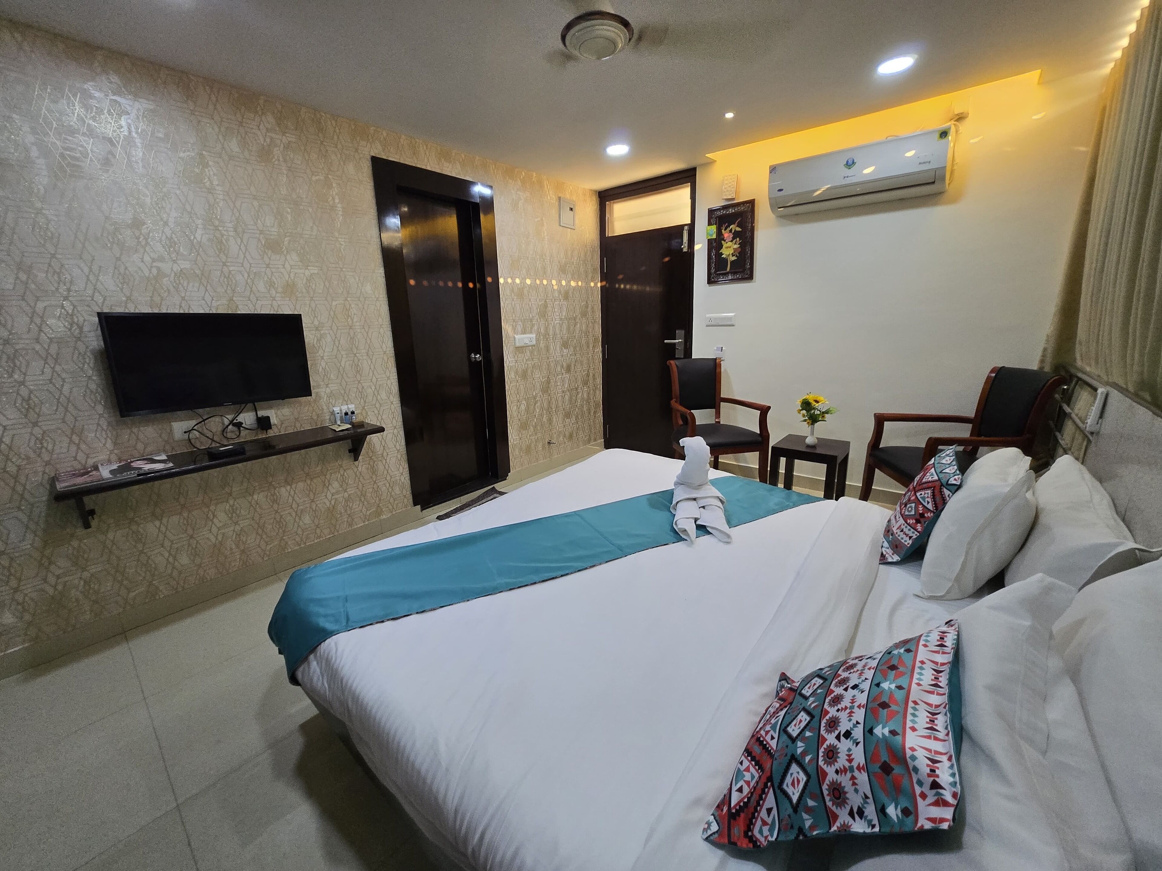 A hotel room with a bed, a TV, a desk, a chair, and an air conditioning unit.