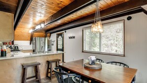 A kitchen with wooden beams, a wooden dining table, and bar stools. - Sleek Blue Lake Springs Retreat w/ Deck & Yard! (Arnold)