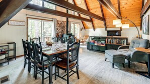 A spacious loft with a high ceiling, exposed beams, and large windows. There is a dining area with a wooden table and chairs, a cozy seating area with a sofa and armchairs, and a fireplace. - Sleek Blue Lake Springs Retreat w/ Deck & Yard! (Arnold)