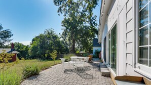 Une terrasse avec un sol en briques, du mobilier d’extérieur et une vue sur une maison dotée de grandes fenêtres.