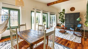 Un coin repas avec une table et des chaises en bois, un hamac et un buffet sombre doté de tiroirs.