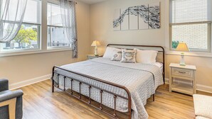 Un dormitorio con una cama, dos mesitas de noche, una silla y una ventana con cortinas.