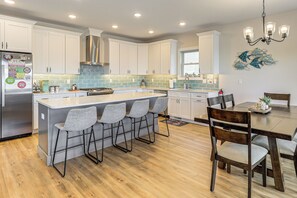 A modern kitchen with white cabinets, a stainless steel refrigerator, and a central island with bar stools. - Walk to Beach & Morey’s Piers: Family Getaway! (Wildwood)