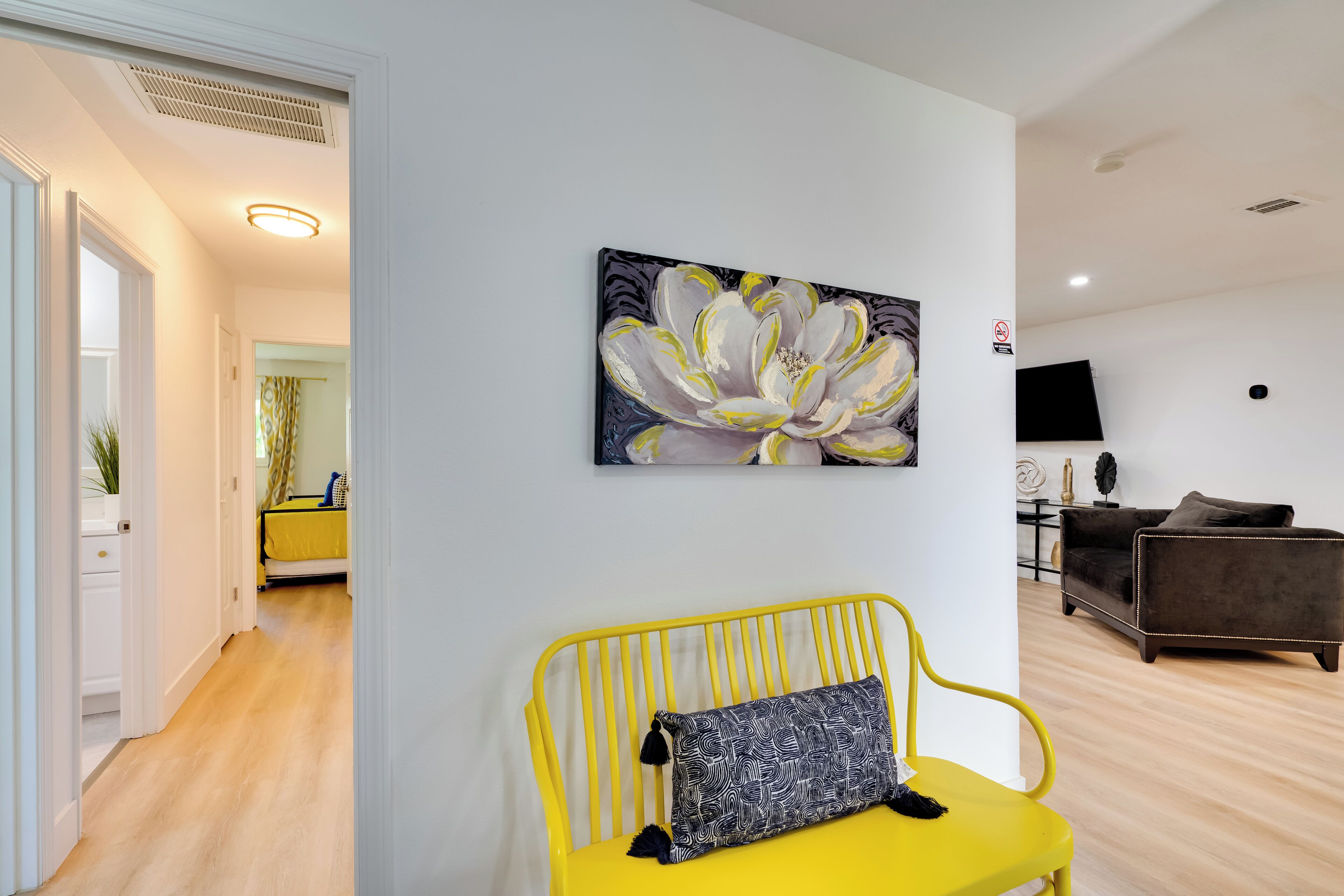 Een moderne woonkamer met een gele bank, een groot bloemen schilderij aan de muur en een donkere bank.