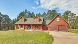 A two-story log cabin with a front porch, a garage, and a well-maintained lawn. - Furnished Deck, Black Hills View: 'Lazy U' Retreat (Custer)