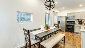 A modern kitchen with stainless steel appliances, a dining area with a wooden table and chairs, and a chandelier. - Walk to Bishop Arts District: Home w/ Deck (Dallas)