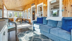 Una habitación acogedora con techo de madera, un sofá azul, una mesa de comedor con sillas y vistas al exterior.