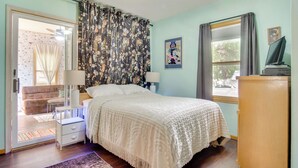 Un dormitorio con cama, mesita de noche, cómoda, ventana con cortinas y puerta que da a un balcón.
