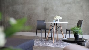 Una sala moderna con una pared de concreto gris, una mesa redonda con un jarrón de flores blancas, dos sillas negras y una planta en maceta sobre una mesa redonda.