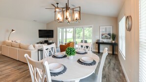 A dining area with a round table, white chairs, and a modern chandelier. - Golf Cart & Preserve View: The Villages Retreat! (The Villages)