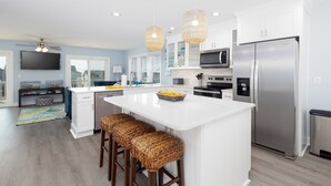 A modern kitchen with white cabinetry, stainless steel appliances, and a central island with stools. - Roof Top Sunsets! Walk to Beach - Bikes - Hot Tub! (Surf City)
