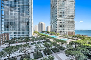 A modern high-rise residential building with a central swimming pool, surrounded by landscaped greenery and a view of the sea.