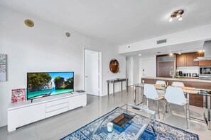 A modern living room with a flat-screen TV, a glass coffee table, and a dining area with a glass table and chairs. - Icon Brickell - Seafront Views - Spa Access (Miami)