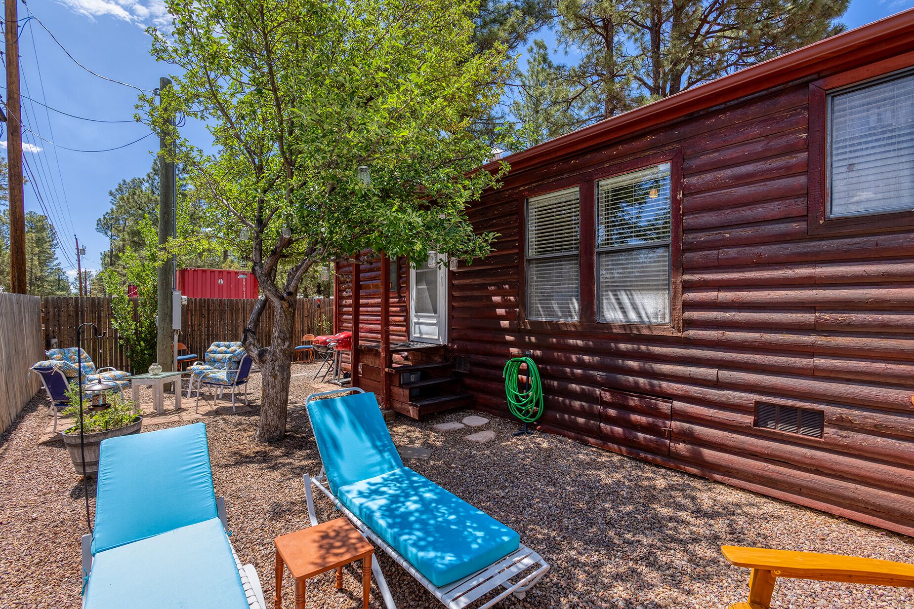 Une cabane dotée d’une terrasse en gravier, de meubles de jardin et d’une clôture en bois.