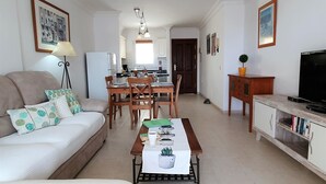 Un salon comprenant un canapé, une table basse et un meuble pour la télévision. Il y a également un coin repas avec une table et des chaises.