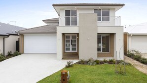 Ein modernes, zweistöckiges Haus mit Garage, Balkon und einem gepflegten Rasen.