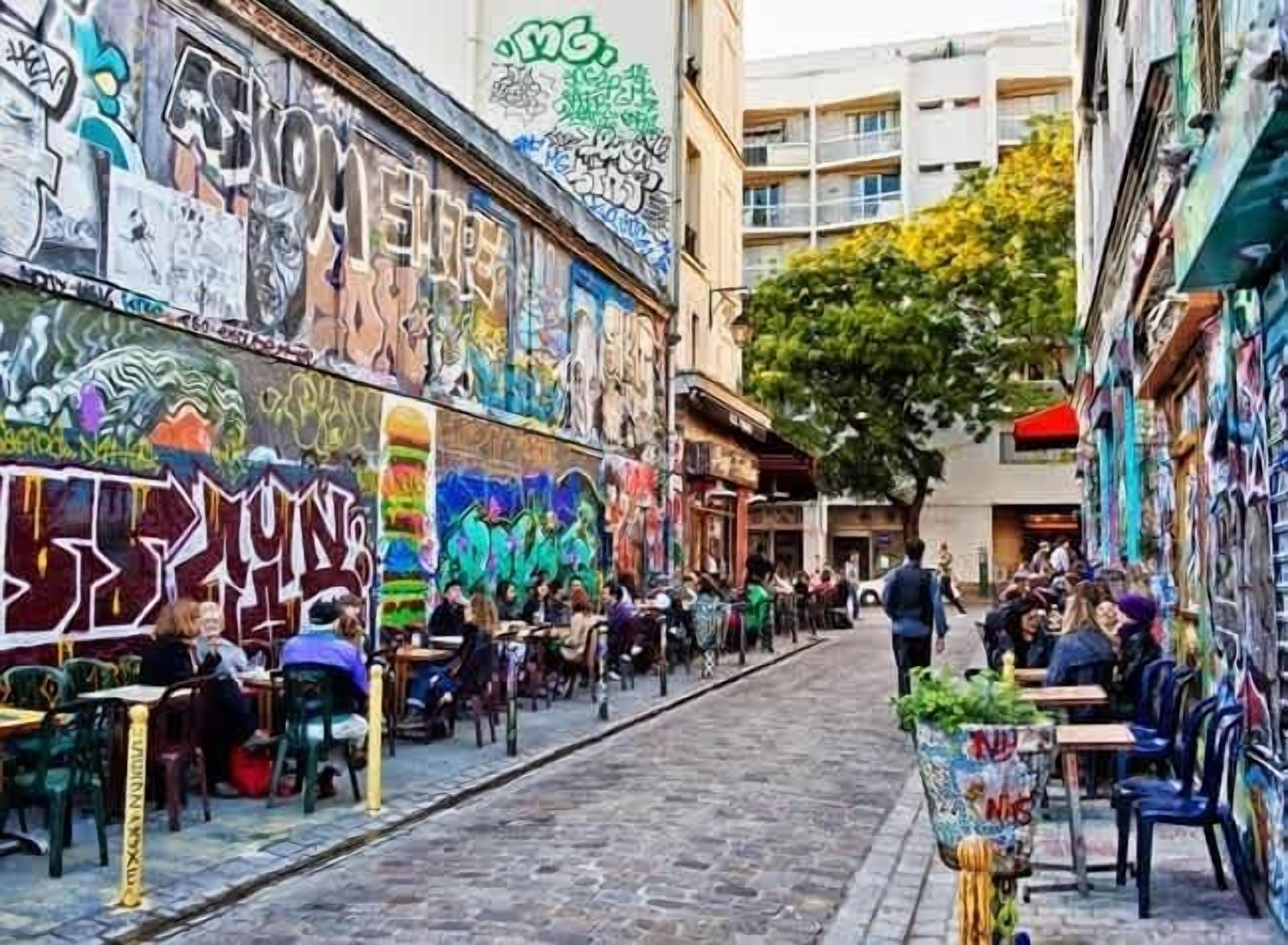 A narrow street with outdoor seating and graffiti-covered walls.
