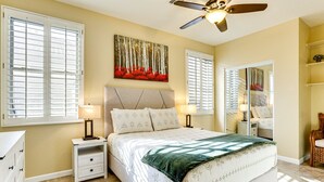 A bedroom with a bed, nightstands, a ceiling fan, and a large window with blinds. - Spacious 5-bedroom house 3 min from Cardinals Stadium and West Gate shopping (Phoenix)