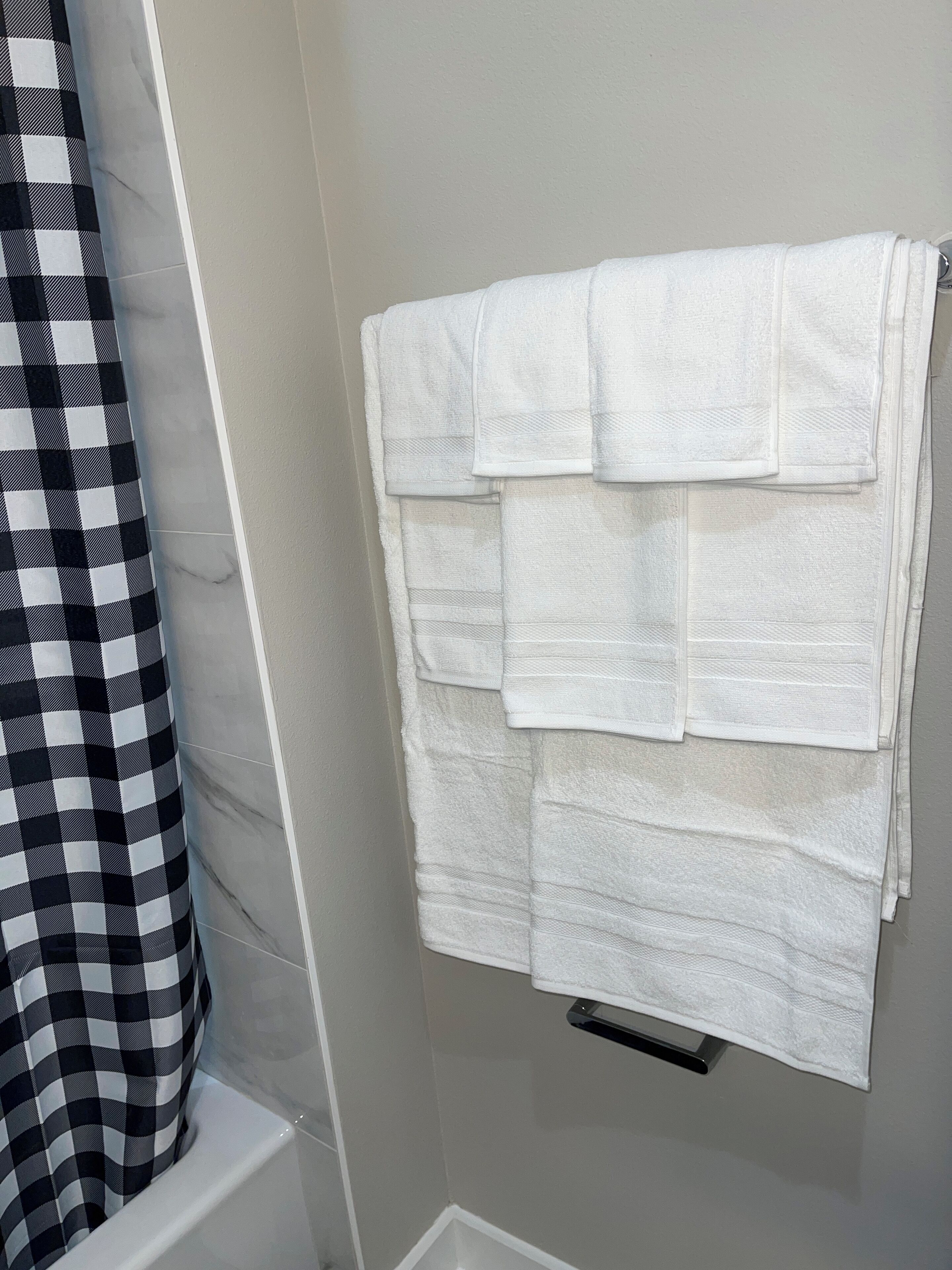 A bathroom with a white towel rack holding several folded towels. A black and white checkered shower curtain is partially visible.