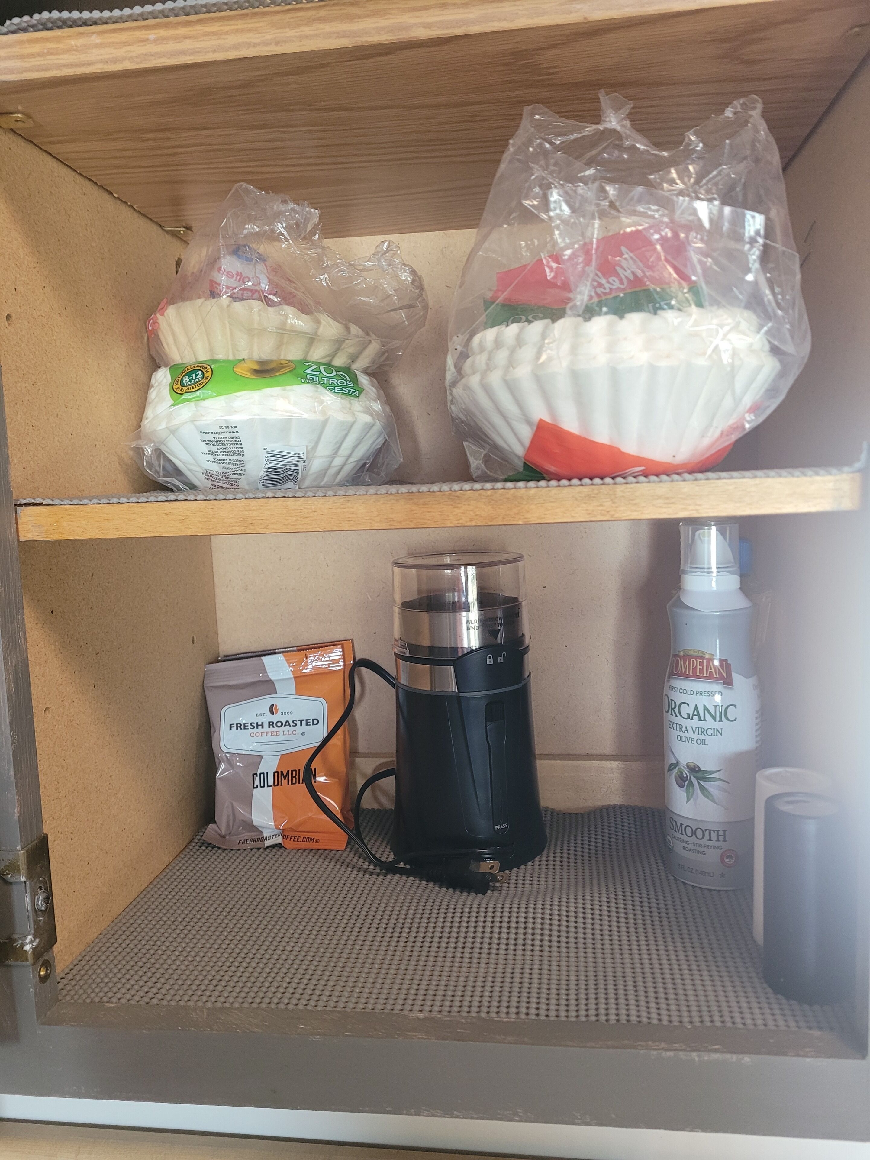 A storage area with shelves containing bags of coffee, a coffee maker, and a bottle of olive oil.