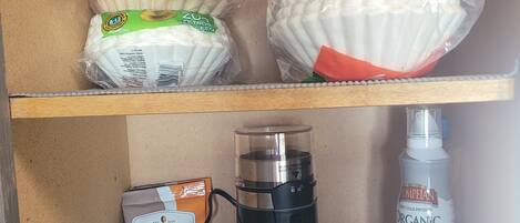 A storage area with shelves containing bags of coffee, a coffee maker, and a bottle of olive oil.