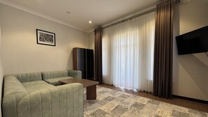 Una sala de estar con sofá, una mesa de centro, un televisor de pantalla plana, un mueble y un ventanal con cortinas.