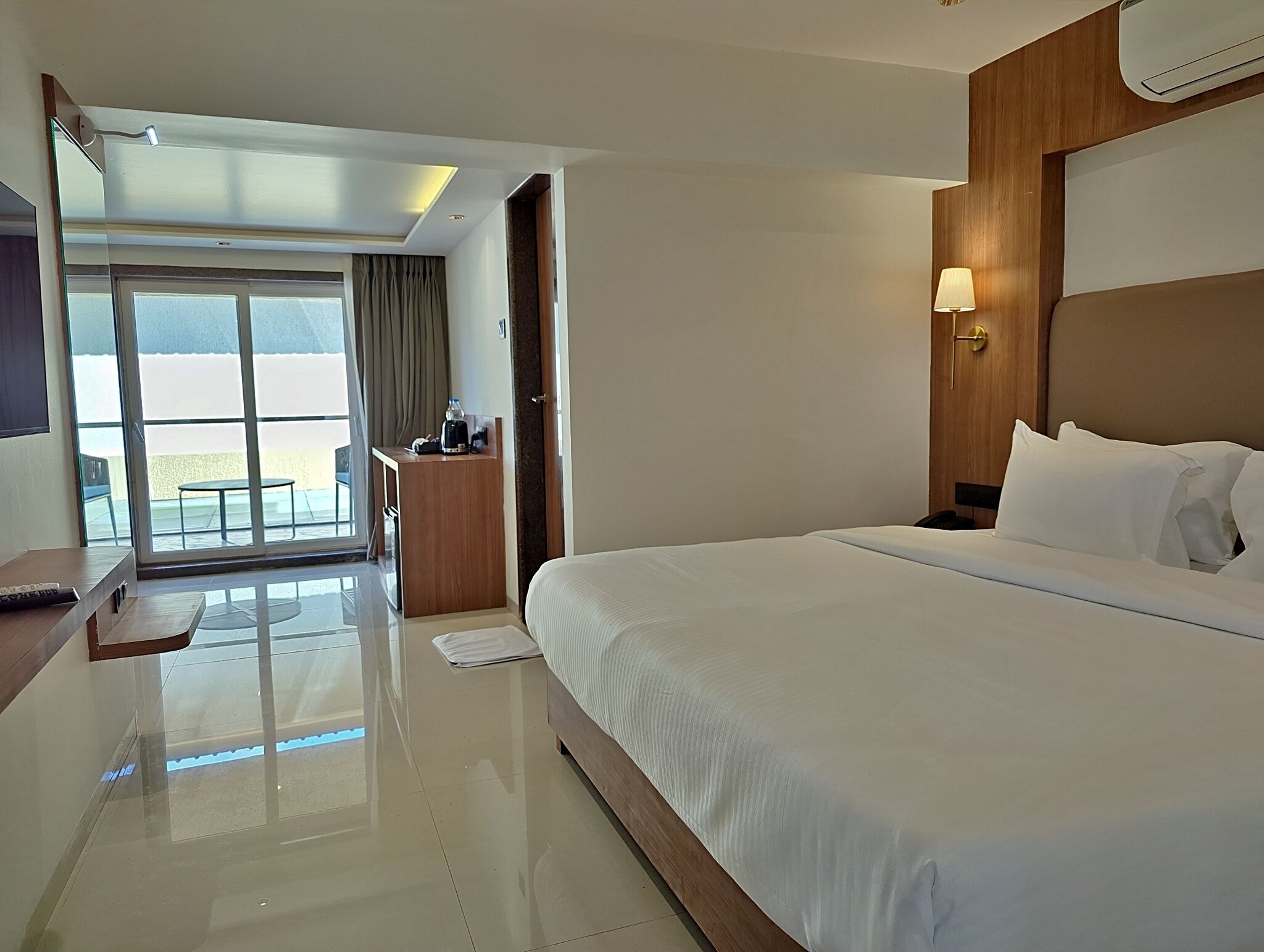 A hotel room with a large bed, a desk, a chair, and a view of the outdoors.