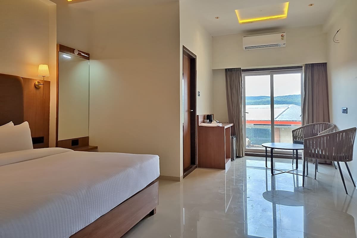 Habitación de hotel con cama, escritorio, silla y un amplio ventanal con vistas.