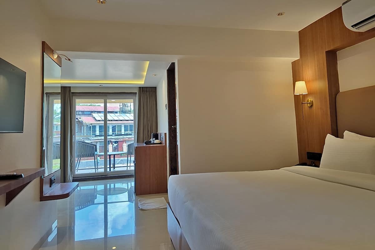 Habitación de hotel con cama, escritorio, silla, televisor y vistas al exterior.