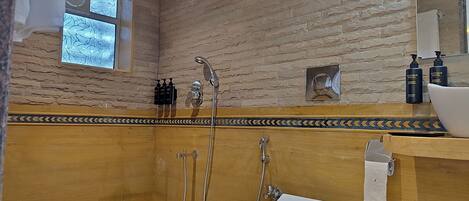 Un baño con ducha, inodoro y lavabo. Se ve una ventana con vistas a árboles, y hay artículos de tocador visibles en la pared.
