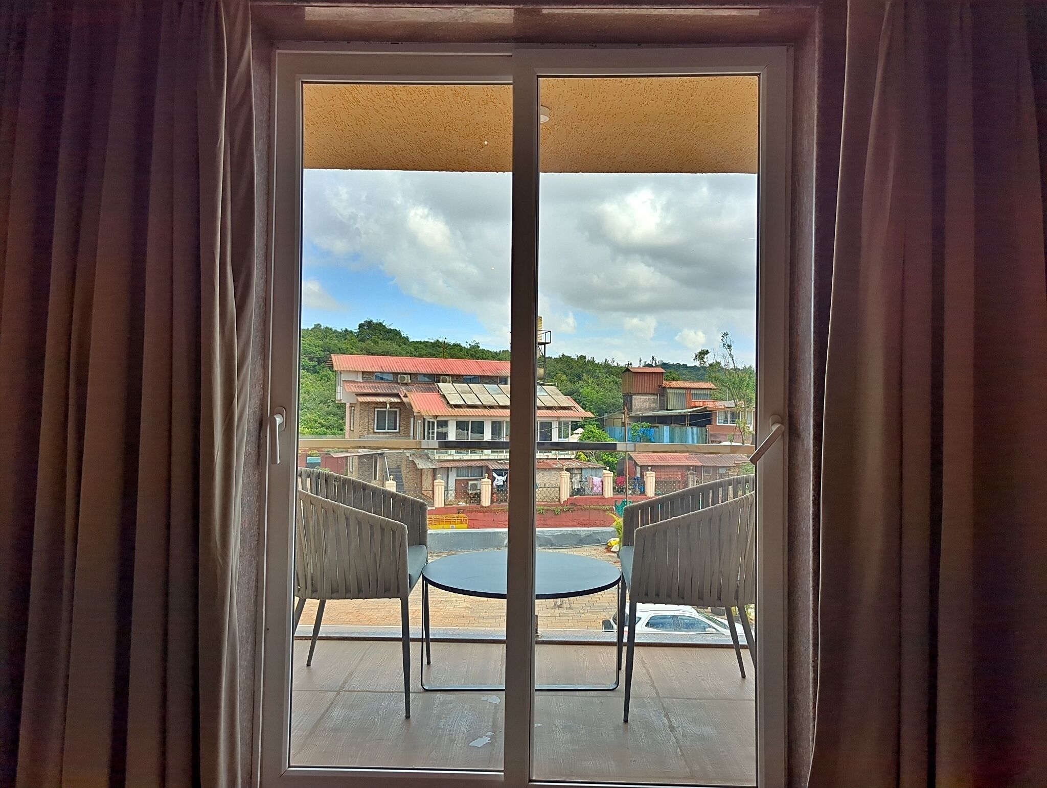 A balcony with two chairs and a table, overlooking a residential area with houses and greenery.