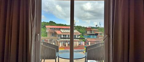 A balcony with two chairs and a table, overlooking a residential area with houses and greenery.