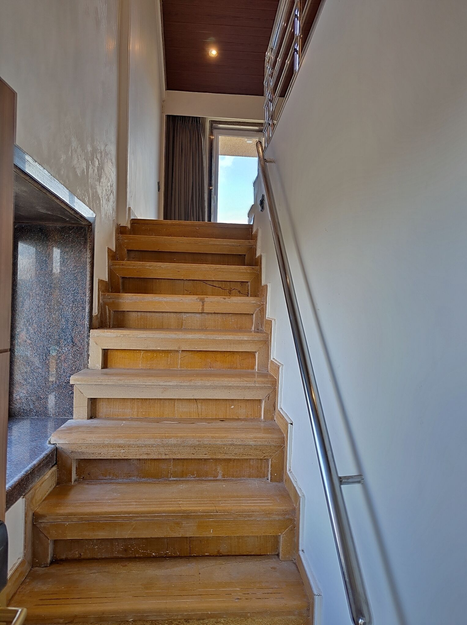 Una escalera de madera con barandilla de metal que lleva a una puerta.