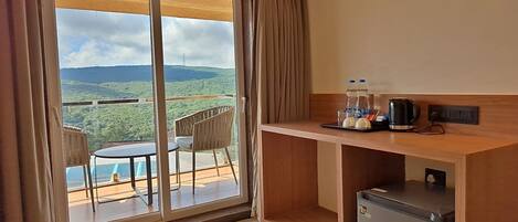 Quarto de hotel com varanda, uma kitchenette compacta e vista para uma paisagem montanhosa.