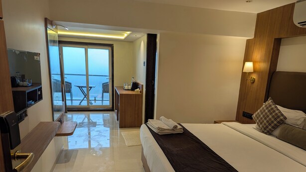 Una habitación de hotel moderna con una cama grande, un escritorio, una silla, un televisor y un balcón con vistas.
