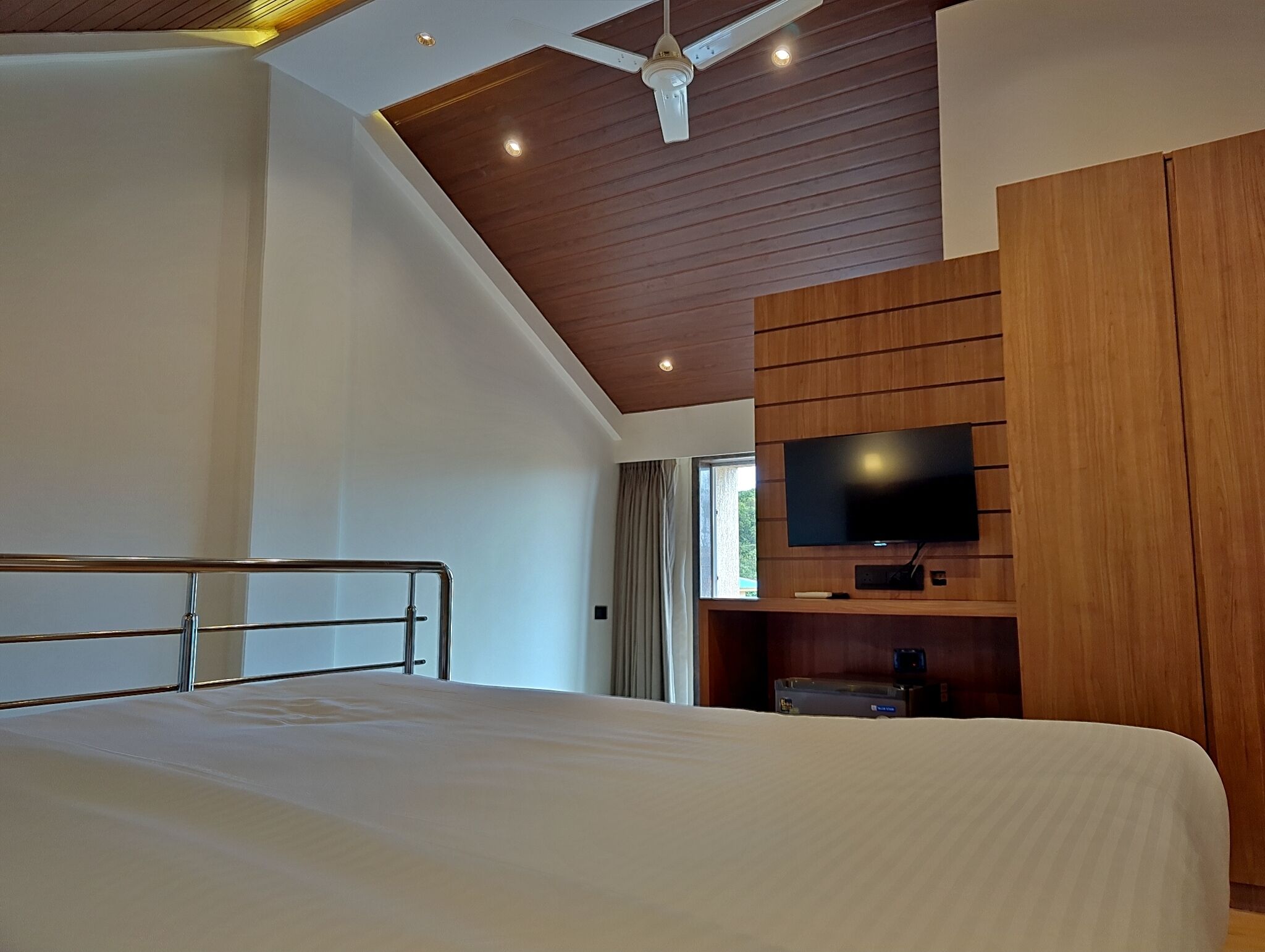 A bedroom with a bed, a ceiling fan, a TV, and a wooden wardrobe.
