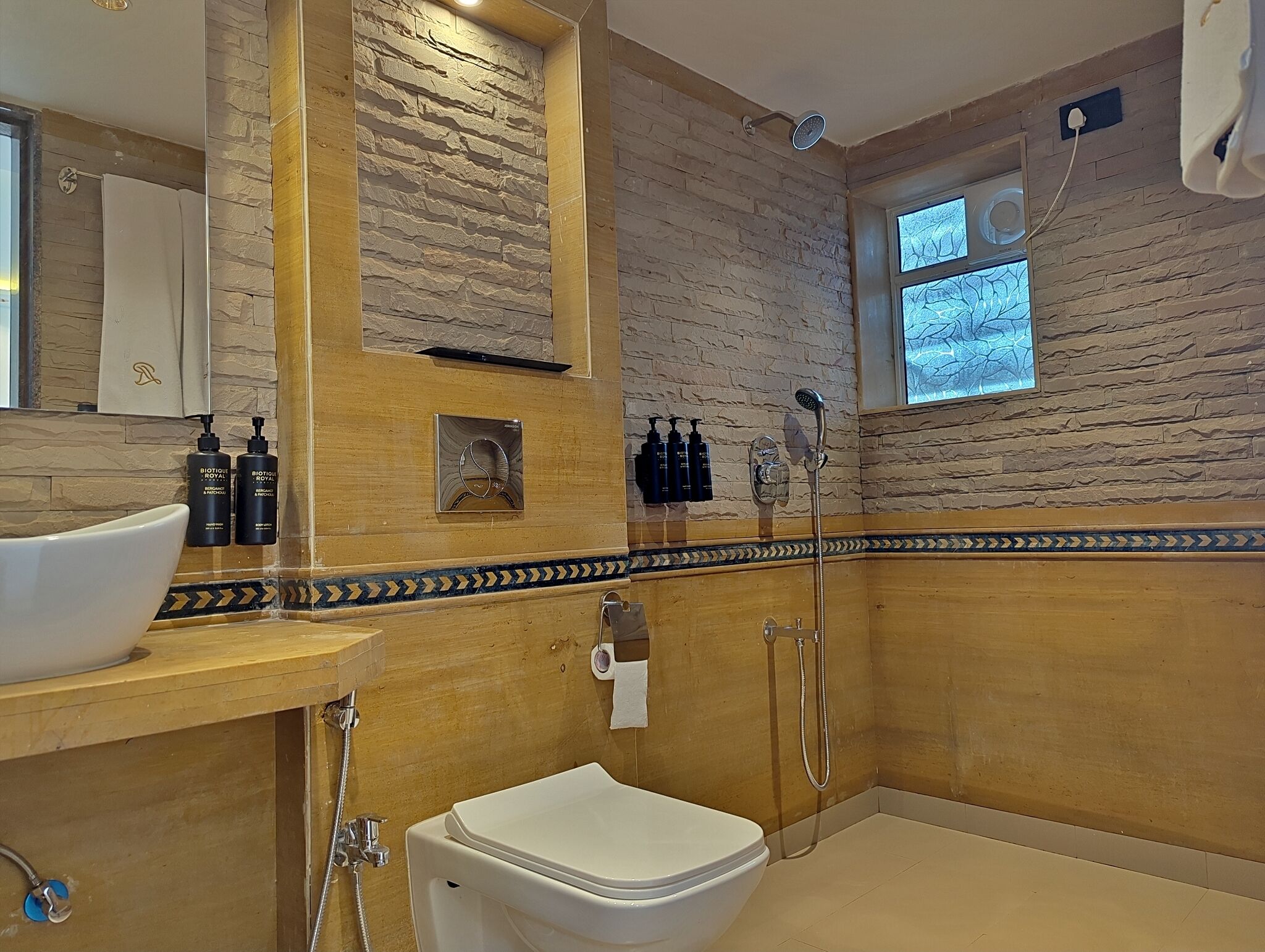 A bathroom with a stone wall, a wooden vanity, a white toilet, and a shower area.