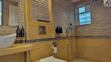 A bathroom with a stone wall, a wooden vanity, a white toilet, and a shower area.