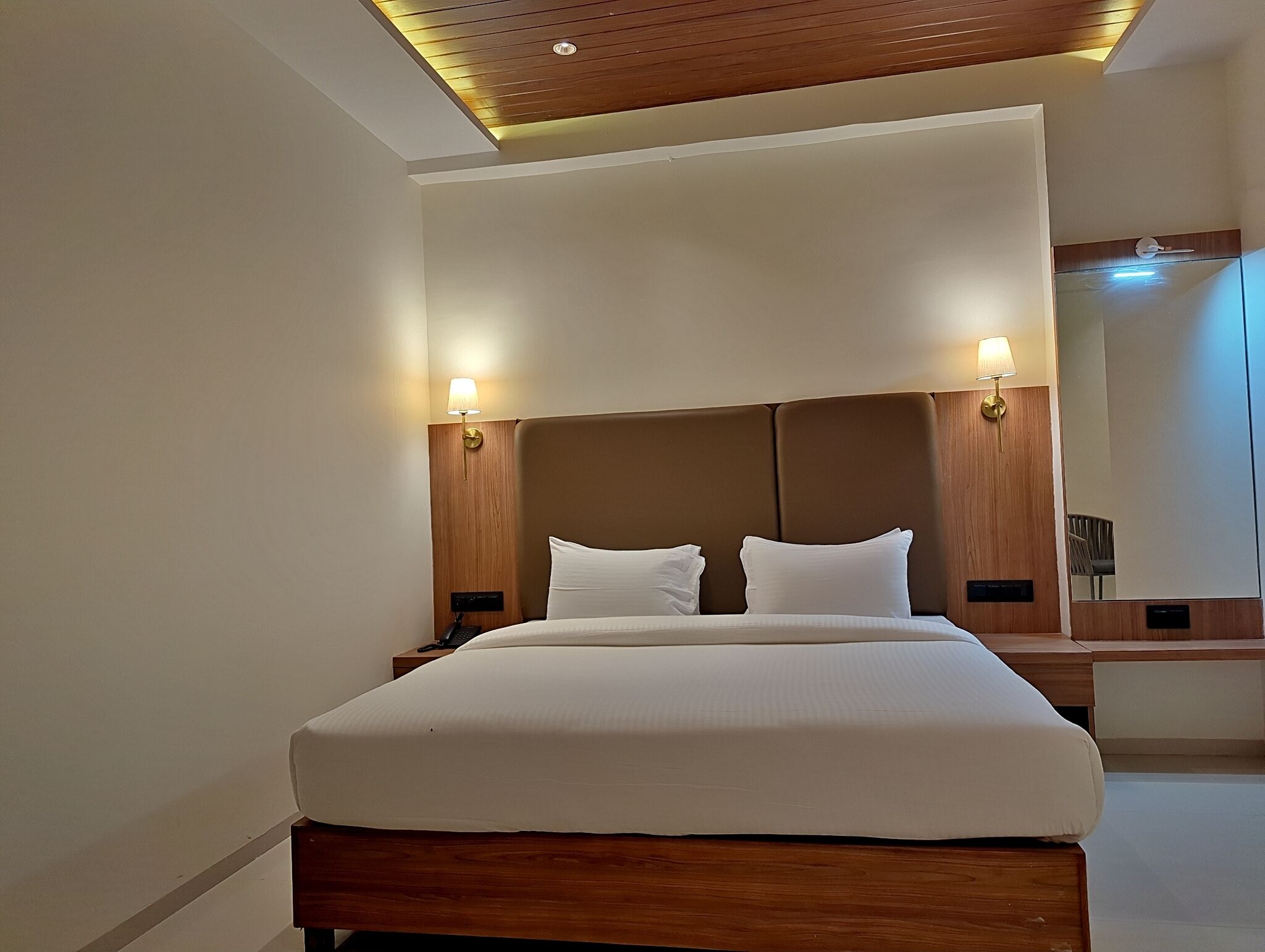 A hotel room with a large bed, wooden headboard, bedside lamps, and a mirror.