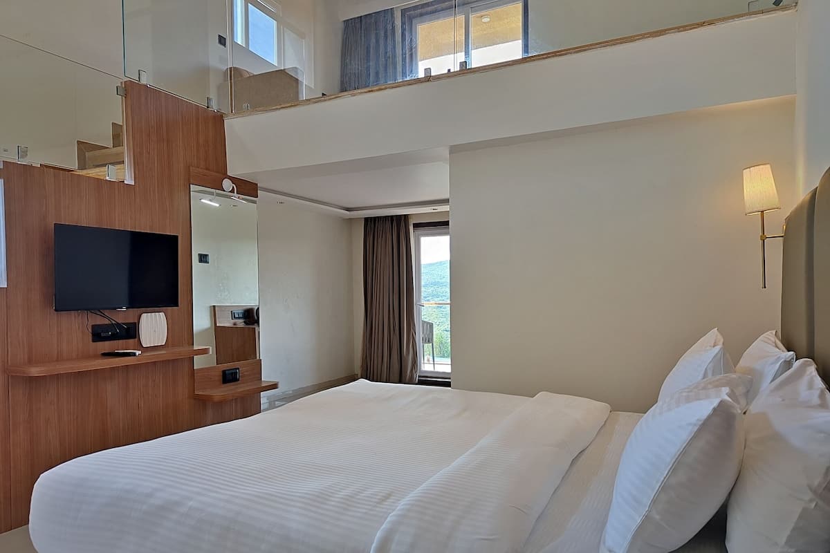 Habitación de hotel con una cama grande, televisión de pantalla plana, un escritorio de madera y un balcón con vistas.