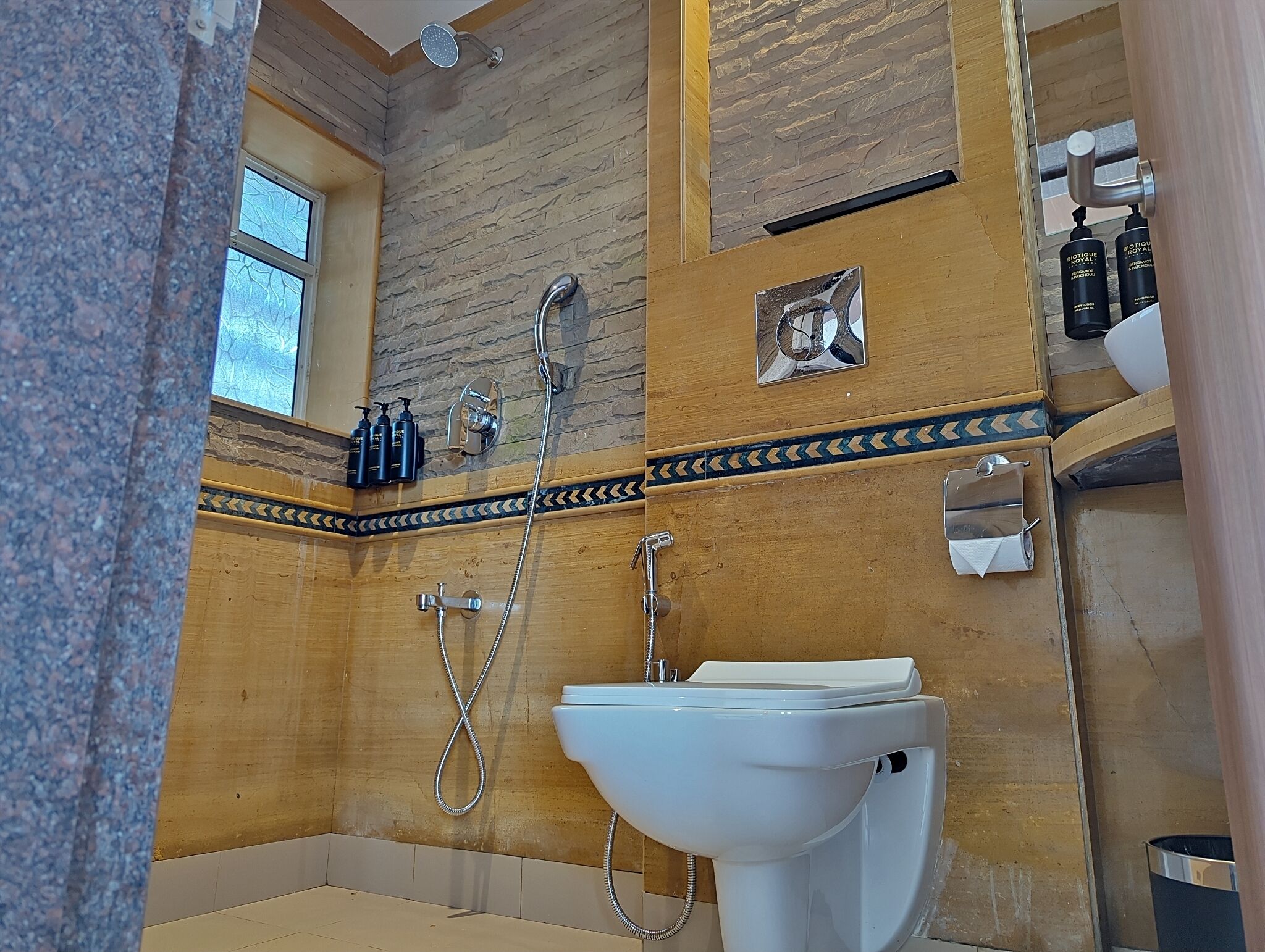 A bathroom with a stone wall, a wooden vanity, a white sink, and a shower.