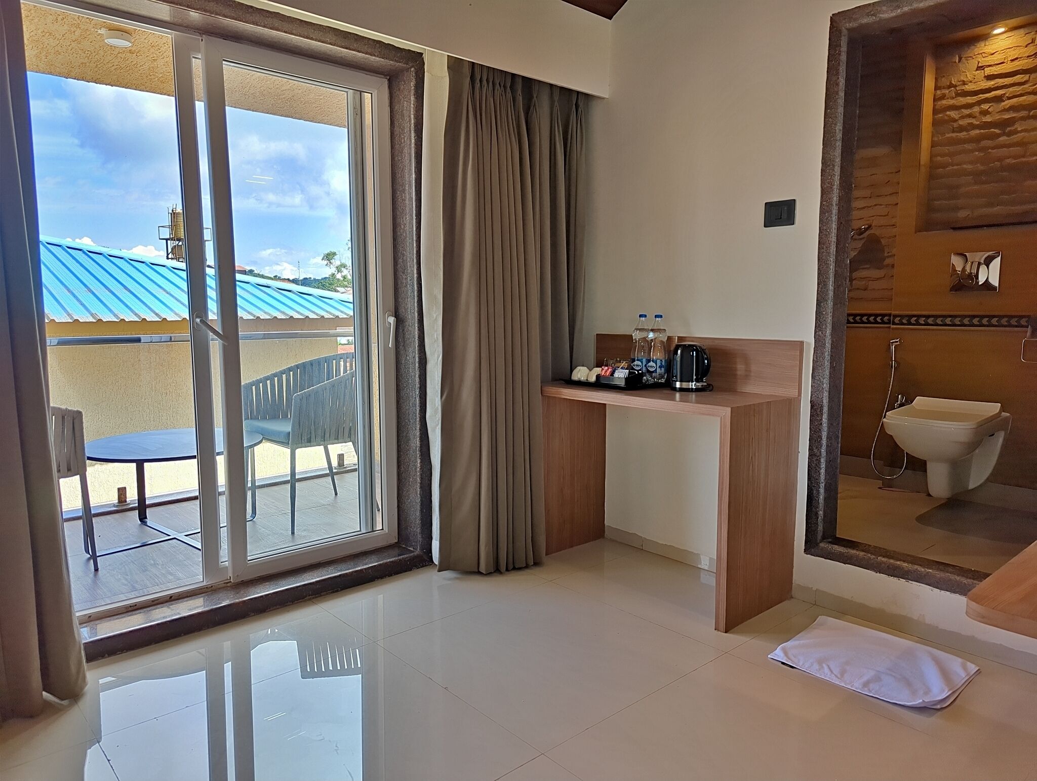 A hotel room with a balcony, a desk with toiletries, and a bathroom with a bidet.