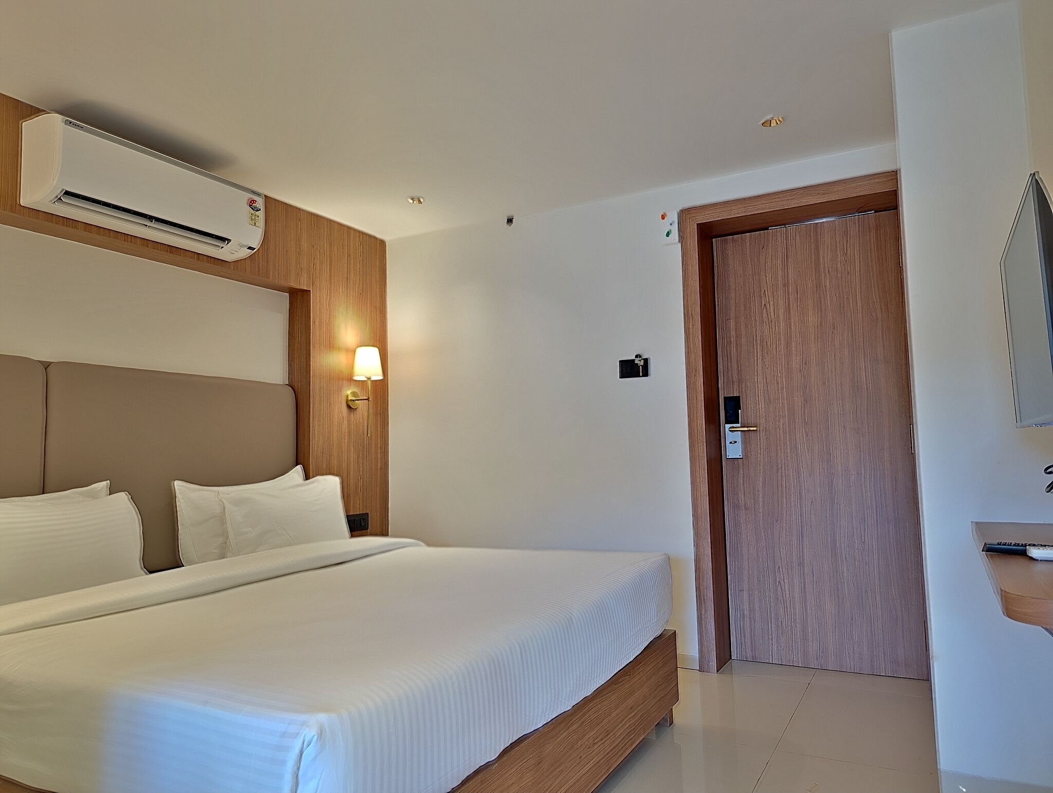 Een hotelkamer met een groot bed, een airconditioning, een houten deur en een wandlamp.
