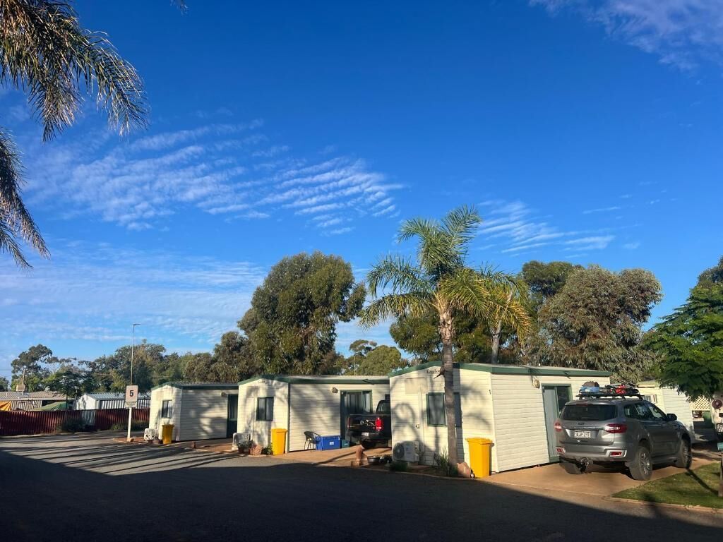 A caravan park with multiple caravan-style buildings, a paved parking area, and a clear blue sky.