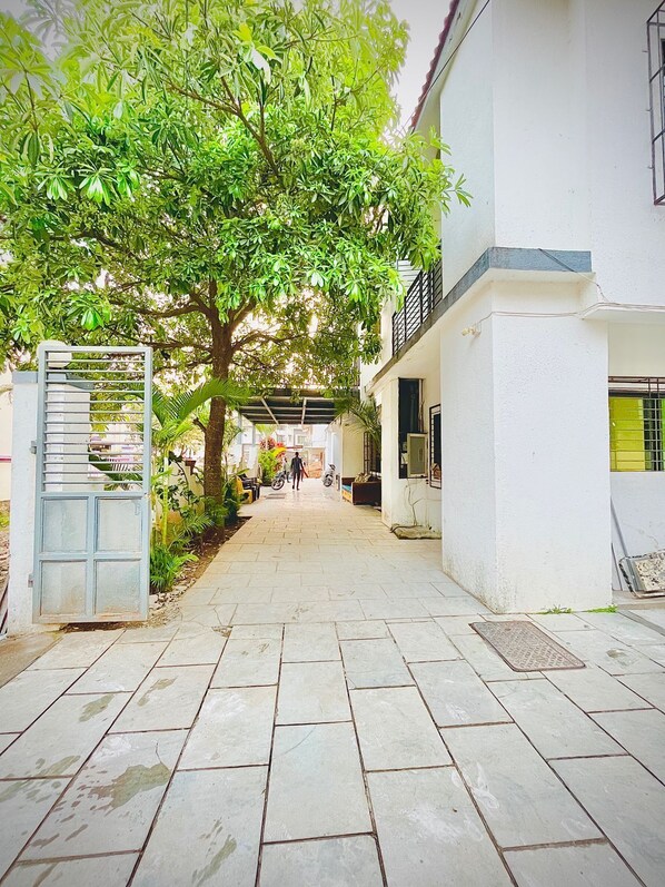 A paved pathway leading to a building with a tree providing shade. - Atharv Villa (Lonavala)