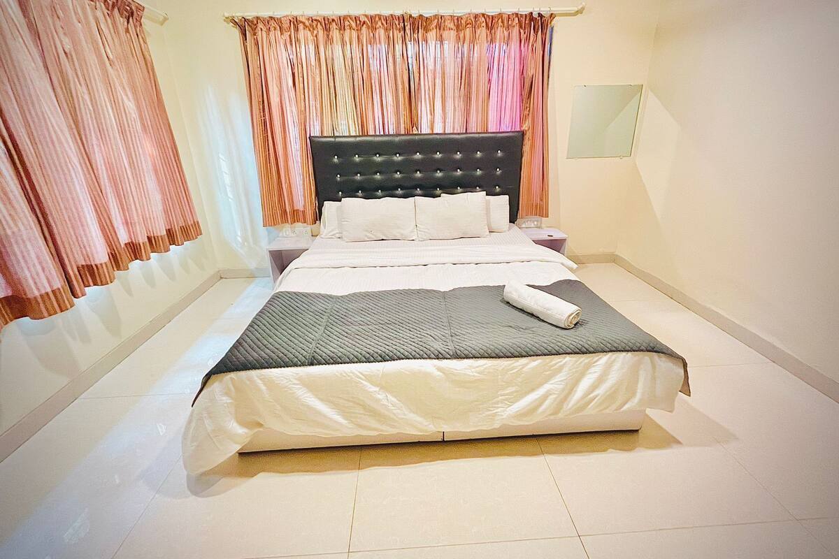 A neatly made bed with a grey quilt, white pillows, and a rolled towel on the footboard.