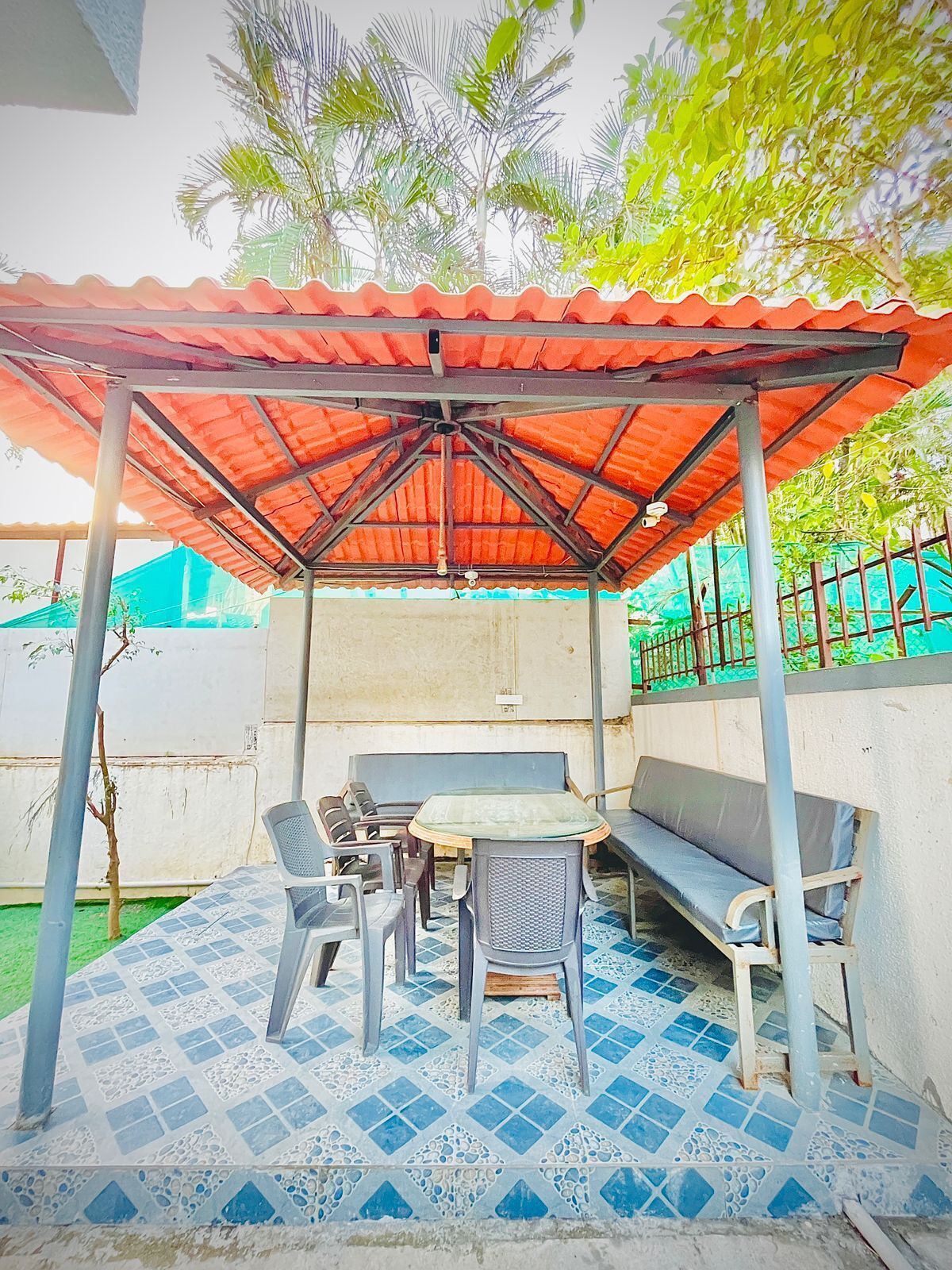 A covered outdoor seating area with a table and chairs, a bench, and a tiled floor.