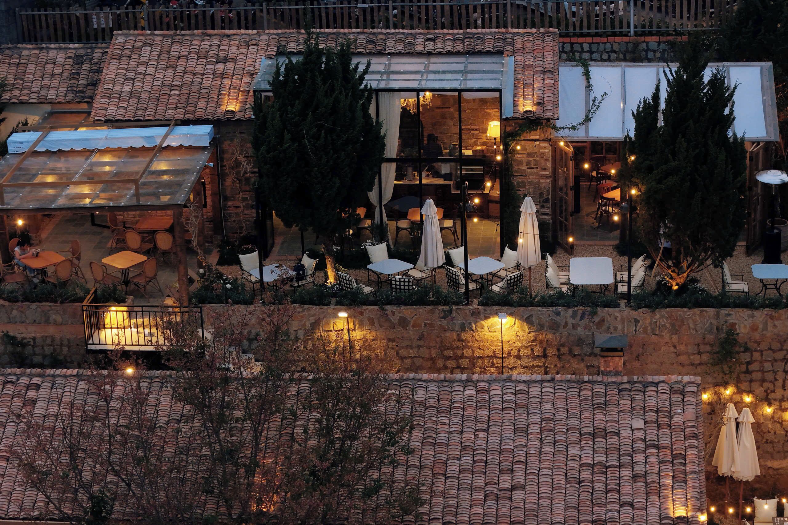 An outdoor dining area with tables and chairs, a stone wall, and a glass enclosure.