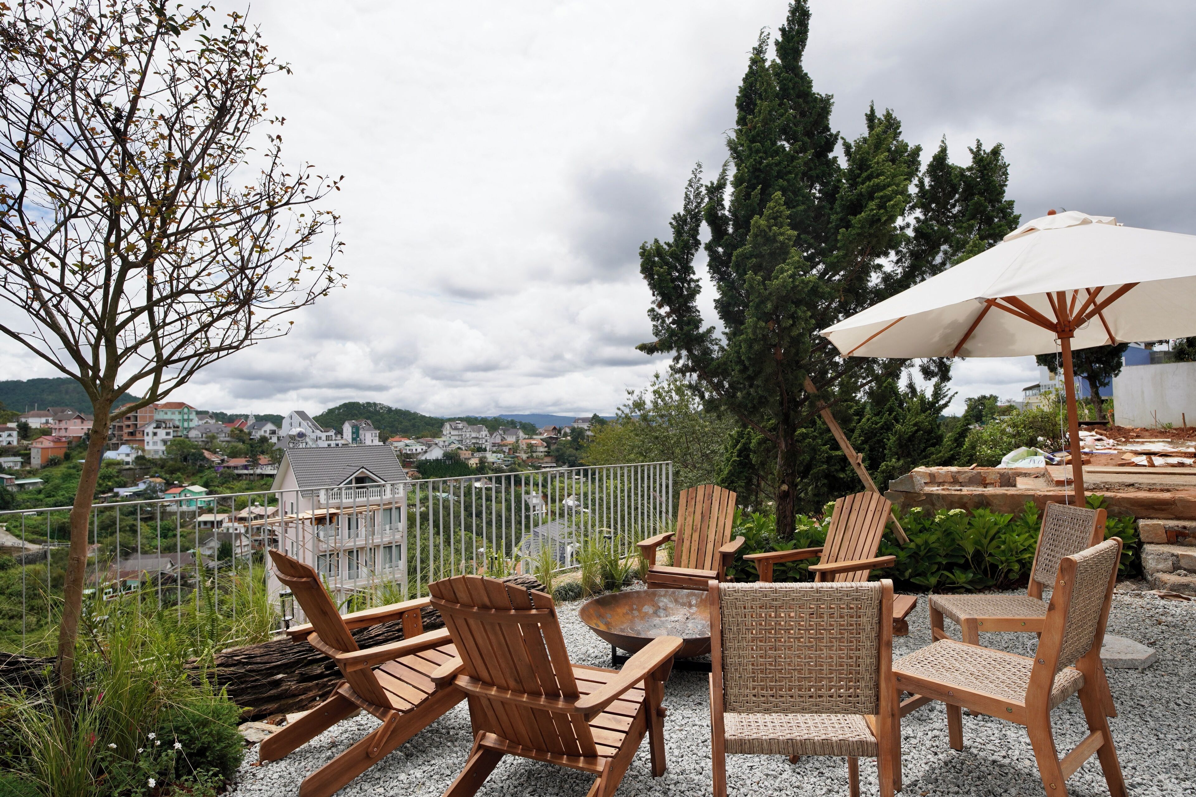 Um terraço com cadeiras e mesa de madeira, com vista para casas e vegetação.