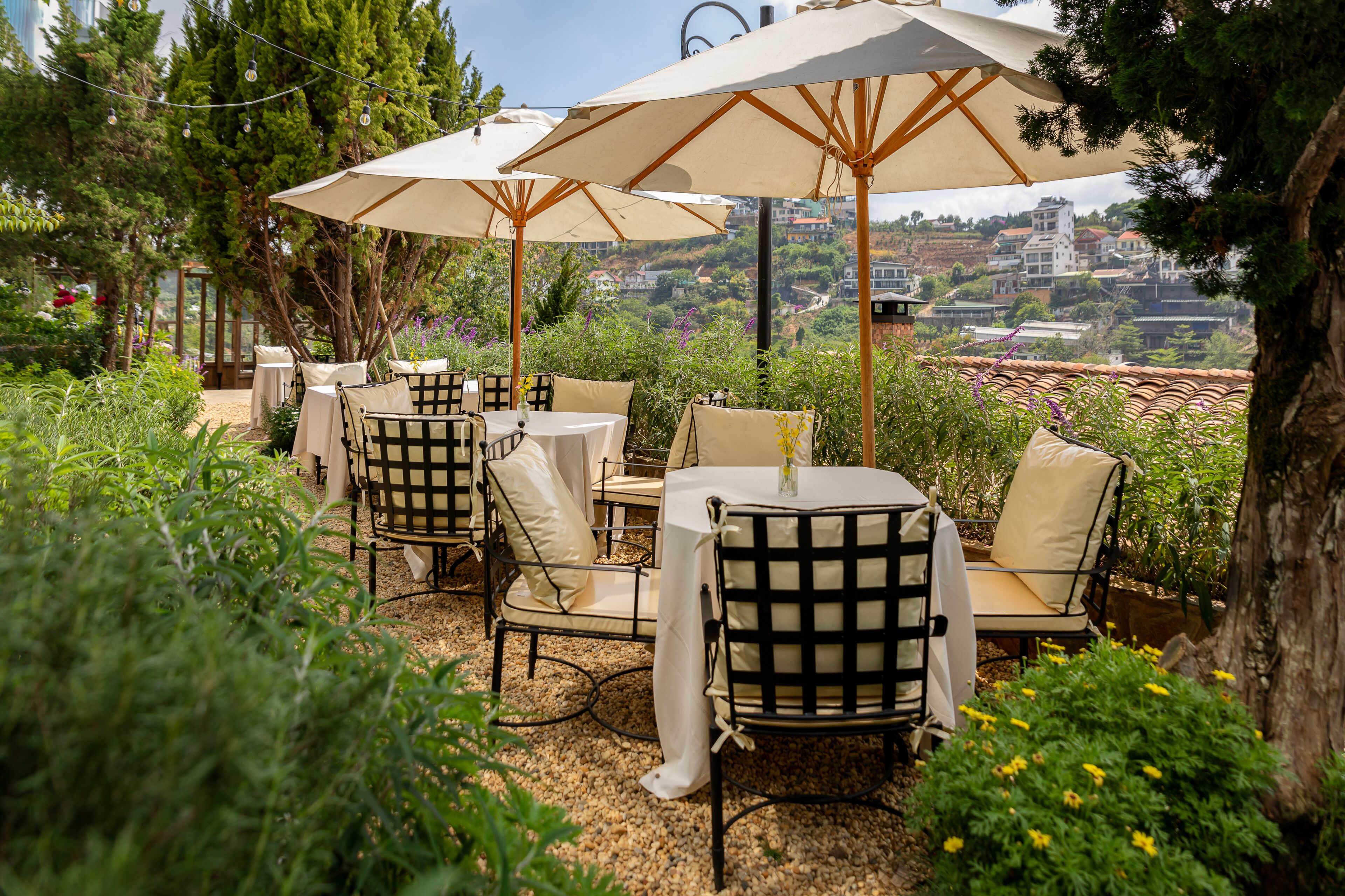 An outdoor seating area with tables and chairs, surrounded by greenery and overlooking a scenic view.